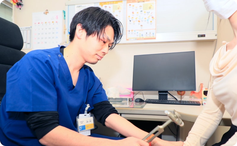 医師が診察室で患者の膝を打腱器で検査している様子