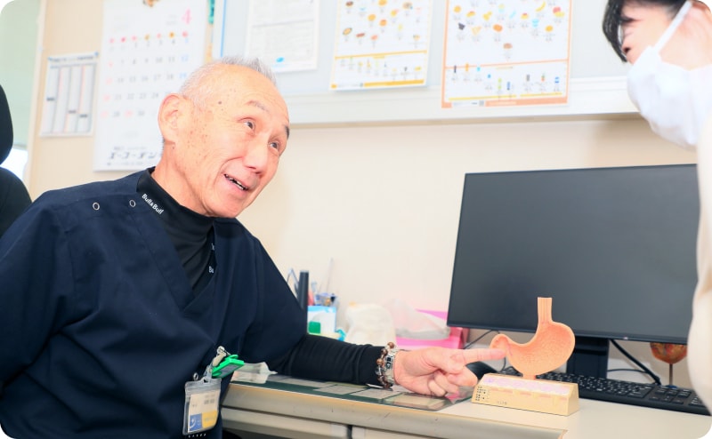 医師が診察室で患者に胃の模型を使って説明している様子