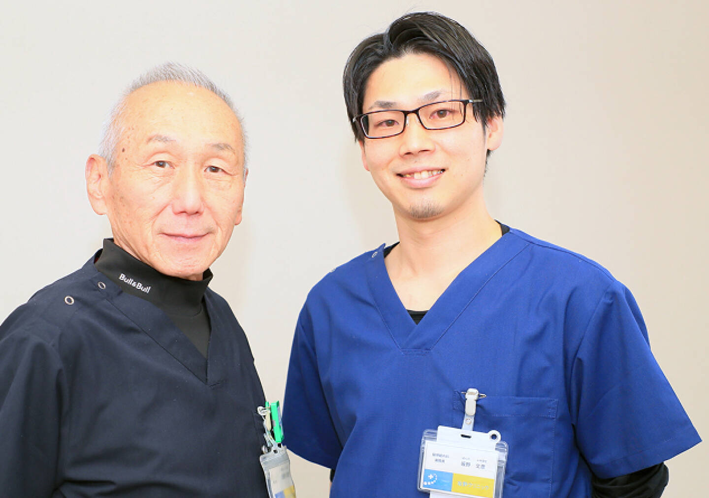 黒と青の医療用ユニフォームを着た2人の医師が並んでいる