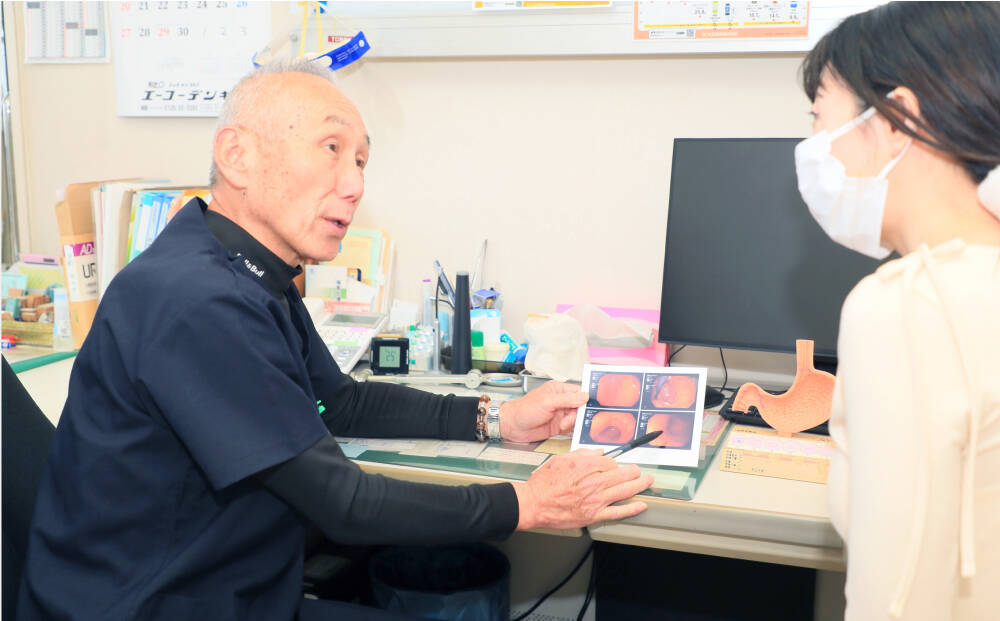 医師が患者に内視鏡画像を見せながら検査結果を説明している診察風景