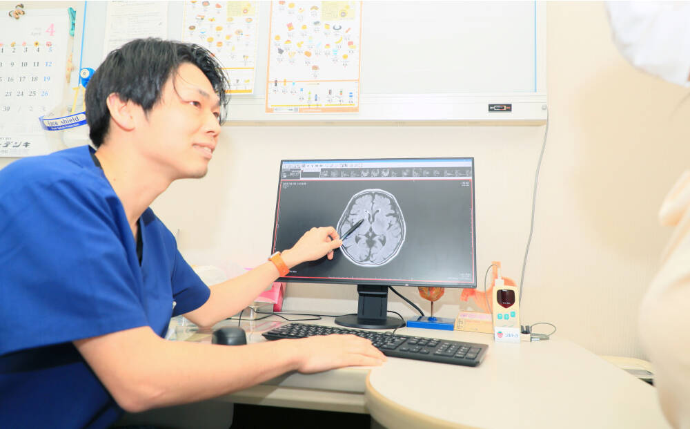 医師が診察室でモニターに映った脳のMRI画像を指しながら患者に説明している様子